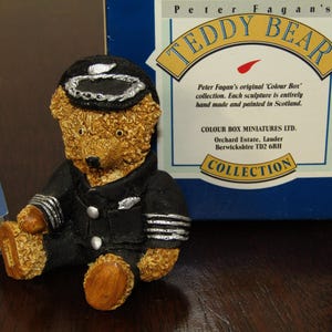 Puede incluir: Una figurita de oso de peluche con uniforme de piloto, con una chaqueta negra, alas plateadas y una gorra negra con una banda plateada. El oso está sentado con las piernas cruzadas y tiene un pelaje marrón. El oso forma parte de la "Colección de osos de peluche de Peter Fagan" y está hecho a mano y pintado en Escocia.