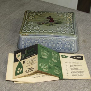 May include: A blue and green porcelain trinket box with a hunting scene on the lid. The box is decorated with shamrocks and accompanied by leaflets detailing Irish porcelain craftsmanship.