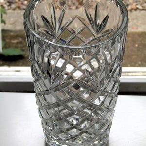 May include: A clear, cut-glass tumbler with a diamond and fan pattern. The glass has a thick base and a slightly flared rim. The intricate design catches the light, creating a sparkling effect. This decorative glass is suitable for beverages.