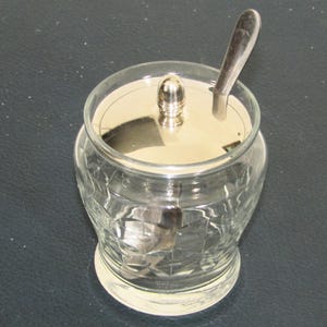 Peut inclure: Un sucrier en verre transparent avec un couvercle argenté et une petite cuillère argentée. Le bol présente un motif en losanges et une base arrondie. Le couvercle a un petit bouton pour soulever. La cuillère est à l'intérieur.