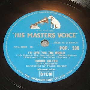 Peut inclure: Un disque vinyle vintage avec une étiquette bleue portant l'inscription "HIS MASTER'S VOICE" et un logo de chien écoutant un gramophone. Le disque présente la chanson "I'D GIVE YOU THE WORLD" de Ronnie Hilton.