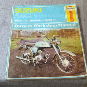 May include: A vintage Suzuki A50P motorcycle owners workshop manual. The cover features a light blue motorcycle with chrome accents, set against a backdrop of a field. The manual's title is in yellow and blue, with the Haynes logo.