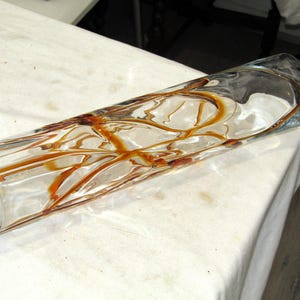 May include: A clear glass vase with brown swirls throughout. The vase is cylindrical and has a rounded bottom.