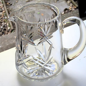 May include: A clear glass jug with a cut glass design. The jug has a handle and a spout.