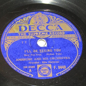Puede incluir: Un disco de vinilo vintage con una etiqueta azul y dorada. La etiqueta presenta el texto "DECCA THE SUPREME RECORD" y el título de la canción "I'LL BE SEEING YOU" de Ambrose and His Orchestra. El disco es negro.