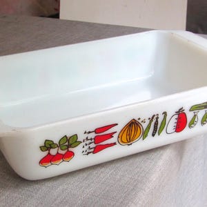 May include: White rectangular baking dish with a vegetable pattern. The dish features a handle on each end and is decorated with illustrations of radishes, peppers, onions, and other vegetables. A vintage kitchen item.