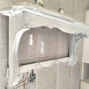 Peut inclure: Étagère murale vieillie, peinte en blanc et gris, avec un bord festonné et des supports décoratifs. Elle comporte des crochets pour suspendre des objets. Dimensions non visibles.