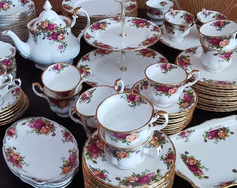 Puede incluir: Juego de té de porcelana blanca con un patrón floral de rosas en tonos rosa y naranja. El juego incluye tazas, platillos, platos, una tetera y una bandeja de varios niveles, todos con ribetes dorados.