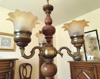 Peut inclure: Un lustre ancien à trois abat-jours en verre dépoli. Le lustre présente une finition en bois foncé et laiton, avec des bras courbes ornés. Les abat-jours ont un bord festonné et le luminaire est suspendu au plafond.