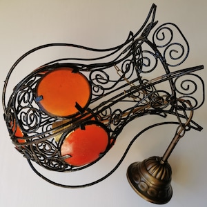 May include: A black metal ceiling light fixture with an ornate design. The fixture has two orange glass shades and a brass chain.