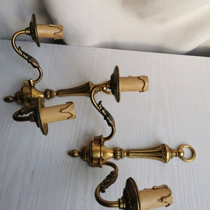 Könnte beinhalten: Drei goldfarbene Wandleuchten mit verzierten Details und weißen Lampenschirmen. Jede Leuchte hat einen gebogenen Arm und einen dekorativen Sockel.
