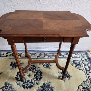 Peut inclure: Petite table en bois antique de couleur marron foncé. Le dessus de la table est incurvé et comporte un tiroir et des pieds décoratifs. La table mesure environ 76 cm de long, 46 cm de large et 71 cm de haut.