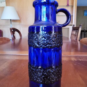 Peut inclure: Un vase en céramique bleu cobalt avec une anse. Le vase présente une bande texturée bleu foncé au milieu. La finition brillante met en valeur la forme et la couleur du vase. Une pièce décorative pour la décoration intérieure.