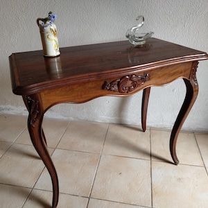 May include: A dark wood antique table with curved legs and ornate carvings. A decorative vase with blue flowers and a glass swan figurine rest on the table's surface. The table is approximately 30 inches long.