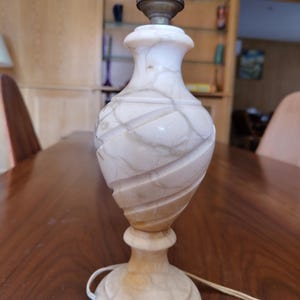 Peut inclure: Une lampe de table décorative à l'aspect marbré. La lampe présente une palette de couleurs beige clair et blanche avec un motif en spirale sur le corps. La lampe a une base ronde et une douille d'ampoule standard.