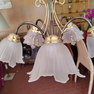 May include: A decorative chandelier with five lights. The fixture has a gold and black finish with curved arms. Each light has a white, tulip-shaped shade. The chandelier is designed for indoor use.