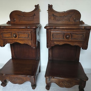 Peut inclure: Une paire de tables de chevet en bois brun foncé, chacune dotée d'un tiroir avec un bouton rond, d'une étagère inférieure ouverte et d'un panneau arrière sculpté avec un bord supérieur incurvé. Les meubles reposent sur quatre pieds sculptés.