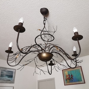 May include: A bronze-colored chandelier with a nature-inspired design. The fixture features four light bulbs, curved arms, and a central bowl. The design incorporates branch-like elements and decorative accents, creating a rustic aesthetic.