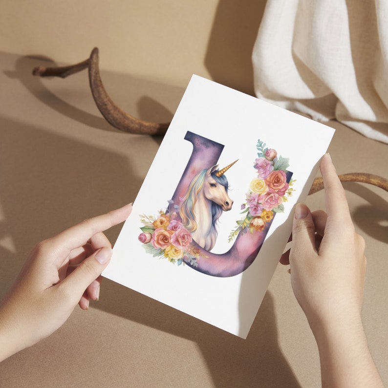 May include: A watercolor illustration of the letter U with a unicorn and flowers. The unicorn is white with a pink mane and tail. The flowers are pink, yellow, and orange.