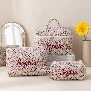 May include: A collection of three floral print cosmetic bags and a matching vanity case. Each item is white with a red floral pattern and embroidered with the name "Sophia". The vanity case has a handle.