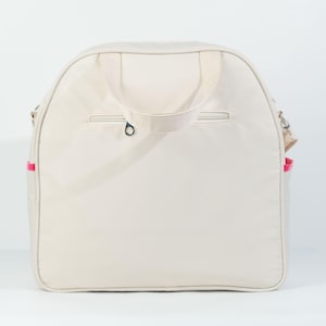 May include: A cream-colored canvas tote bag with a zippered pocket on the front and a pink trim around the edges. The bag has two top handles and a shoulder strap.