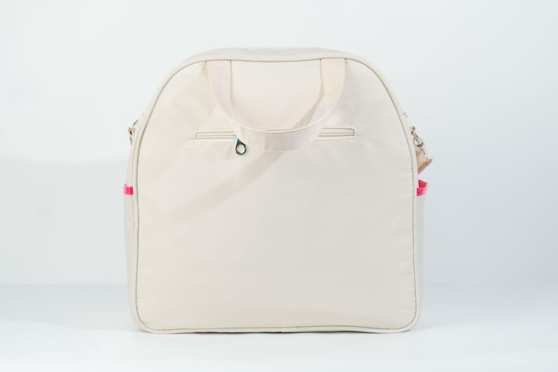 May include: A cream-colored canvas tote bag with a zippered pocket on the front and a pink trim around the edges. The bag has two top handles and a shoulder strap.