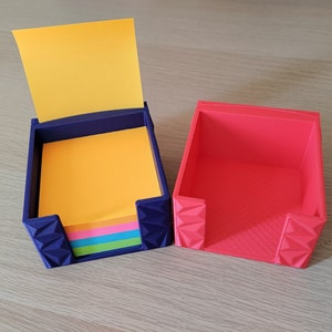 May include: Two empty note paper holders, one is blue and the other is red. Both have a geometric design and are made of plastic.