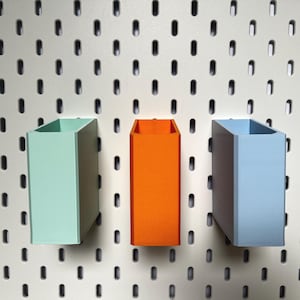 Peut inclure: Trois contenants de rangement muraux en vert menthe, orange et bleu clair. Les contenants sont en plastique et ont une forme rectangulaire.