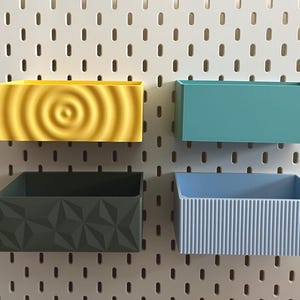 Peut inclure: Quatre bacs de rangement muraux avec différents motifs texturés. Les bacs sont jaunes, turquoise, vert foncé et bleu clair.
