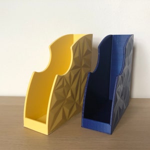 May include: Two geometric patterned magazine holders, one yellow and one blue, on a wooden surface.