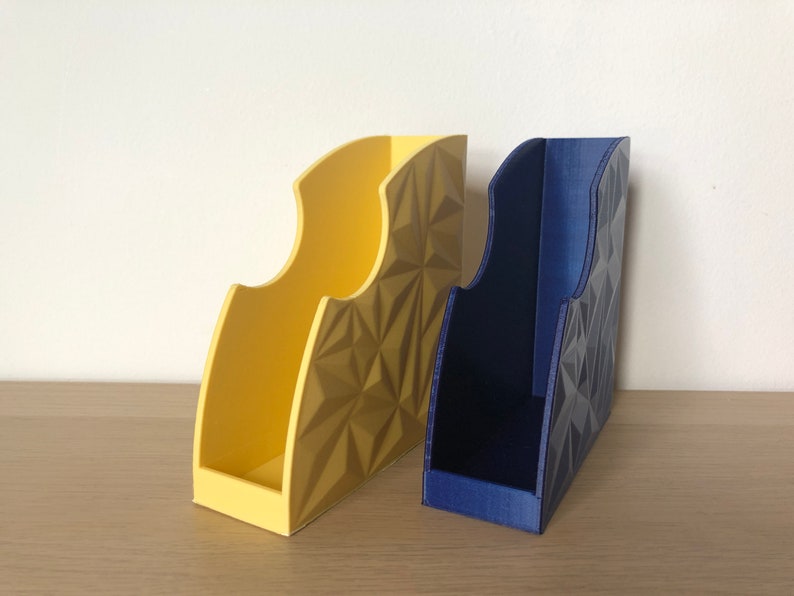 May include: Two geometric patterned magazine holders, one yellow and one blue, on a wooden surface.