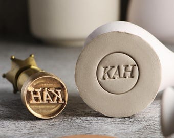 May include: A close-up of two brass stamps with the words "HAX" and "KAH" engraved on them. The stamps are on a light grey surface.
