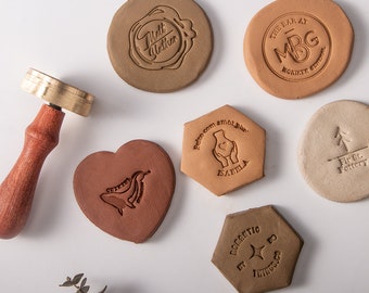 May include: Six different clay stamps with various designs. The stamps are in different shapes, including a heart, a hexagon, and a circle. The designs include a whale, a hand holding a heart, a tree, and a star.