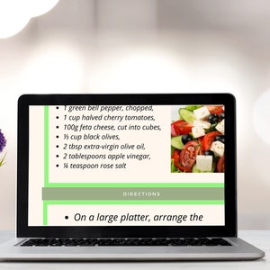 May include: A laptop screen displaying a recipe for a Greek salad. The recipe includes ingredients like green bell pepper, cherry tomatoes, feta cheese, black olives, extra-virgin olive oil, apple vinegar, and rose salt. The directions instruct the user to arrange the salad on a large platter.