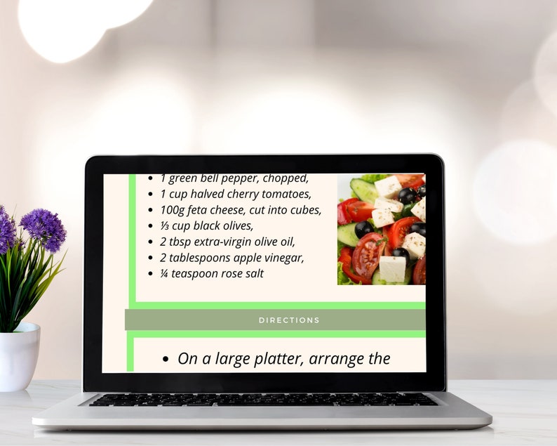 May include: A laptop screen displaying a recipe for a Greek salad. The recipe includes ingredients like green bell pepper, cherry tomatoes, feta cheese, black olives, extra-virgin olive oil, apple vinegar, and rose salt. The directions instruct the user to arrange the salad on a large platter.