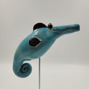 Könnte beinhalten: Eine blaue Keramik-Seepferdchen-Figur mit schwarzen Details, die auf einem Holzsockel mit einer Metallstange steht.
