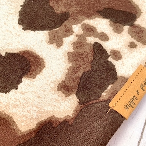May include: A brown and white cow print fabric with a brown leather tag that says "Skippy & Pepper".