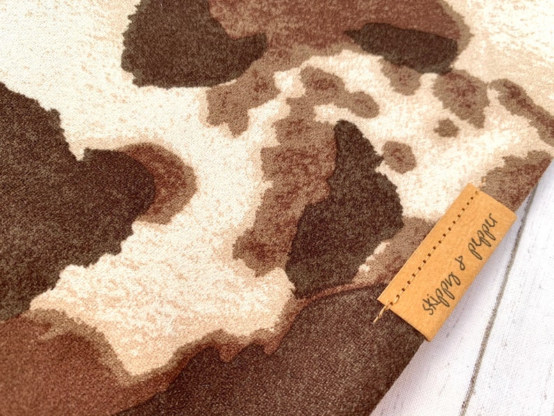 May include: A brown and white cow print fabric with a brown leather tag that says "Skippy & Pepper".