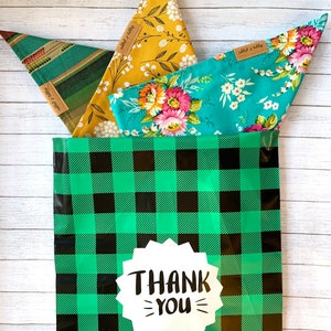 May include: Three fabric bandanas with floral patterns in a green and black checkered gift bag with a white sticker that says "THANK YOU".