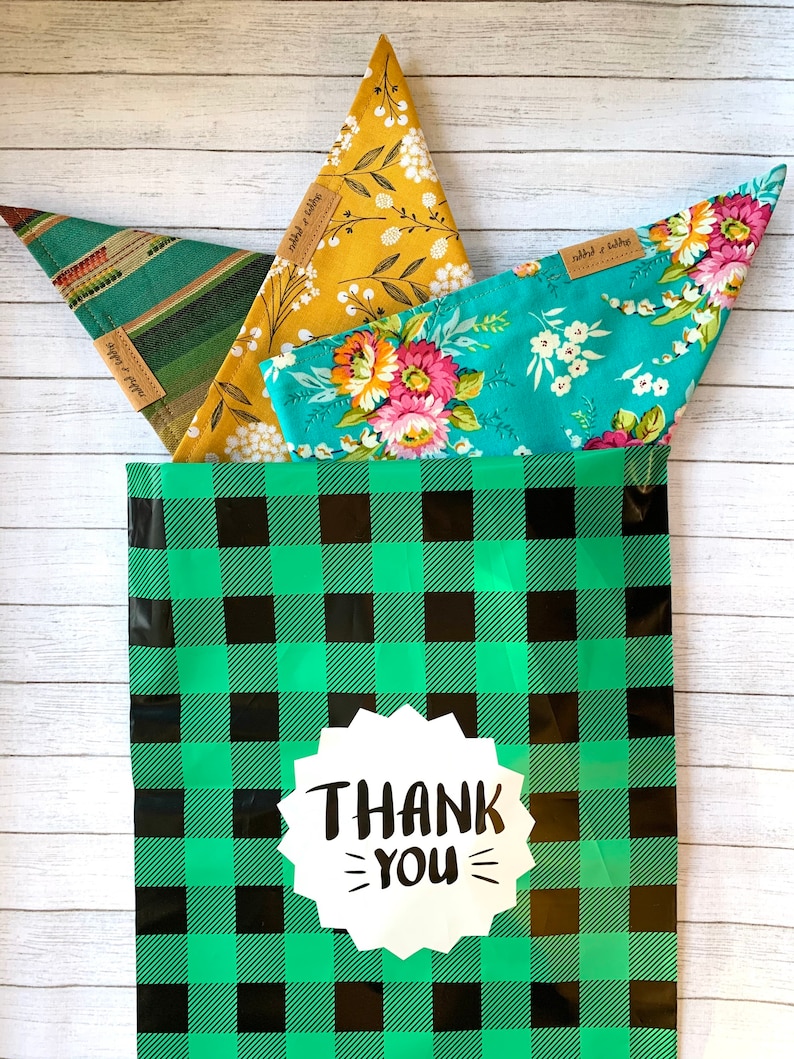 May include: Three fabric bandanas with floral patterns in a green and black checkered gift bag with a white sticker that says "THANK YOU".