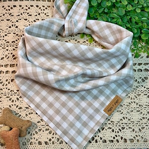 May include: A beige and white gingham dog bandana with a brown leather tag that says "Happy & Free".