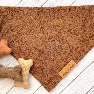 May include: Brown paisley patterned dog bandana with a brown leather tag that says "Snuggles & Piggies".