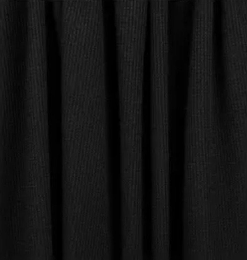 May include: Black fabric with a textured, ribbed surface. The fabric is draped and folded, creating soft folds and shadows.