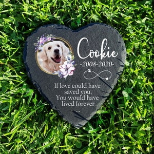 May include: Black heart-shaped slate stone memorial with a photo of a golden retriever in a gold frame. The stone has the text "Cookie - 2008-2020 -" and "If love could have saved you, you would have lived forever..."