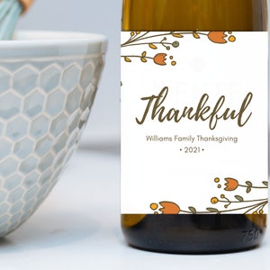May include: A white wine bottle with a label that says "Williams Family Thanksgiving - 2021" and "thankful" in brown cursive lettering. The label is decorated with orange and green floral illustrations.