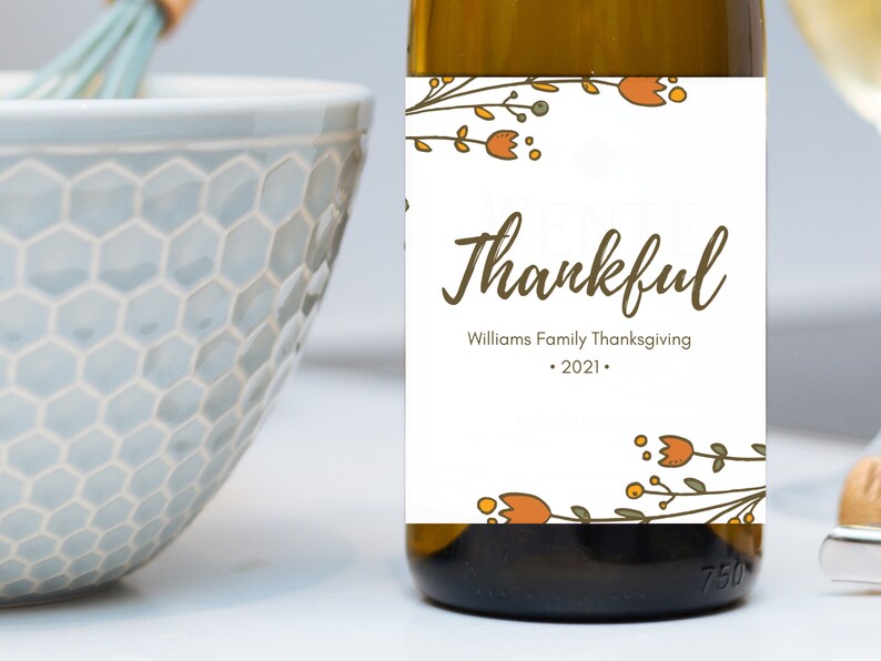 May include: A white wine bottle with a label that says "Williams Family Thanksgiving - 2021" and "thankful" in brown cursive lettering. The label is decorated with orange and green floral illustrations.