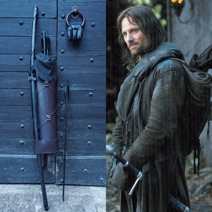 Pode incluir: Um estojo de couro marrom com uma alça preta e flechas, um arco preto e uma espada preta. O estojo está pendurado em uma porta de madeira azul.