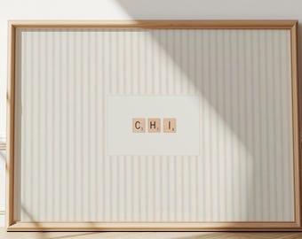 May include: A framed print featuring the letters "C, H, I" spelled out with Scrabble tiles. The print is set against a striped background and framed in a light wood. The artwork is displayed on a wall with a wooden floor.
