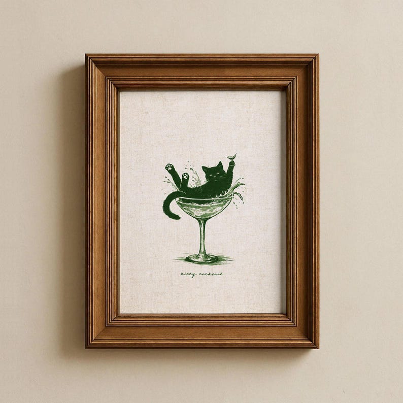 May include: A framed print featuring a green illustration of a black cat lounging in a martini glass. The cat is surrounded by splashes, with the words "kitty cocktail" below the glass. The frame is made of brown wood.
