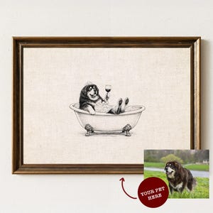 May include: A framed black and white line art print featuring a dog sitting in a clawfoot bathtub filled with bubbles, holding a wine glass. Below the frame, a smaller photograph shows a brown and black dog standing in a grassy field.